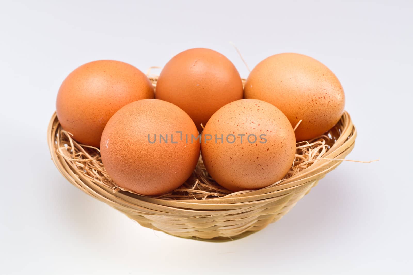 five brown eggs in rattan basket isolated on whte surface