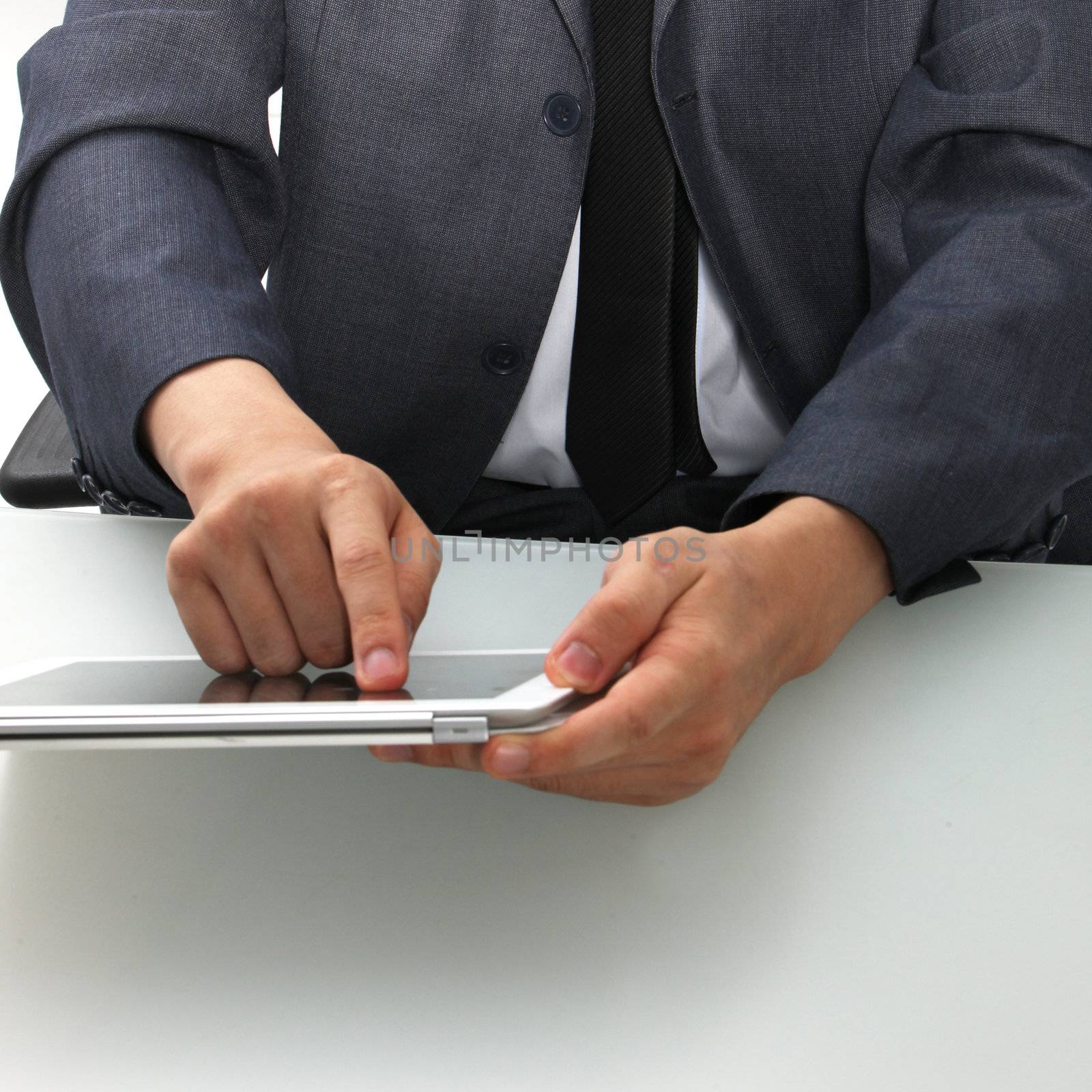 Cropped view of the torso and hands of a man seated at a desk using a tablet computer touching the screen with his finger