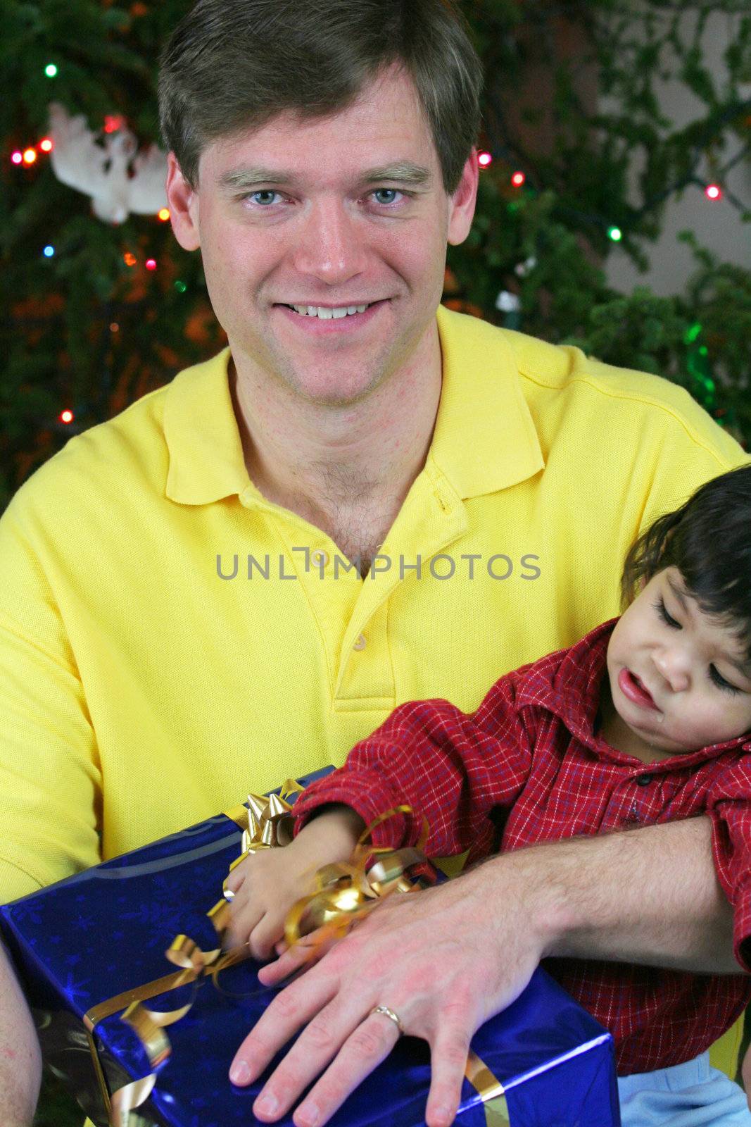 Happy father holding his baby boy by Christmas tree with presents.Baby is  Part Asian, Scandinavian heritage, father is caucasian.