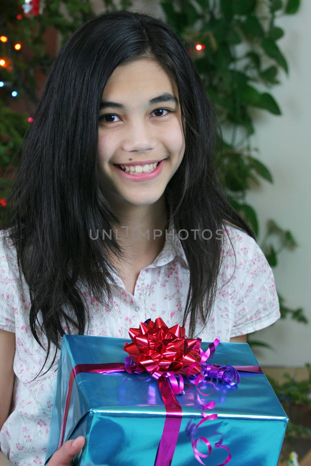 Happy young teenage girl holding her Christmas presents by the Christmas tree. Part Asian, Scandinavian heritage.