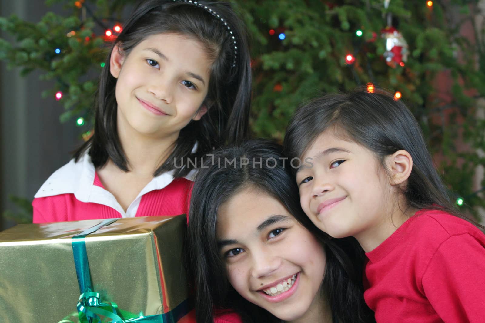 Three happy sisters holding their Christmas presents by the Christmas tree. Part Asian, Scandinavian heritage.