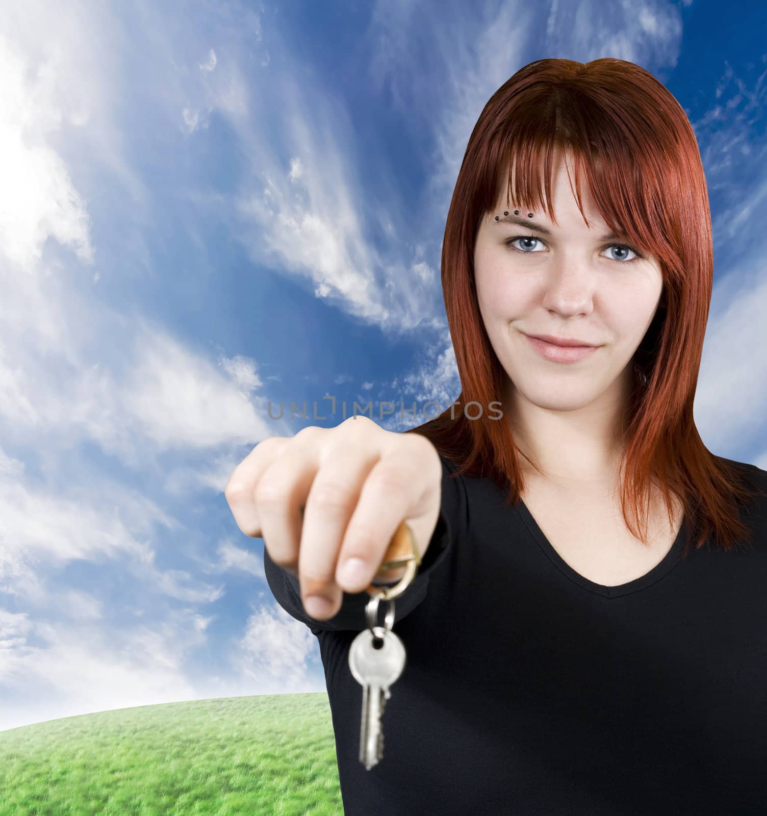 Cute smiling redhead girl holding keys towards the camera.