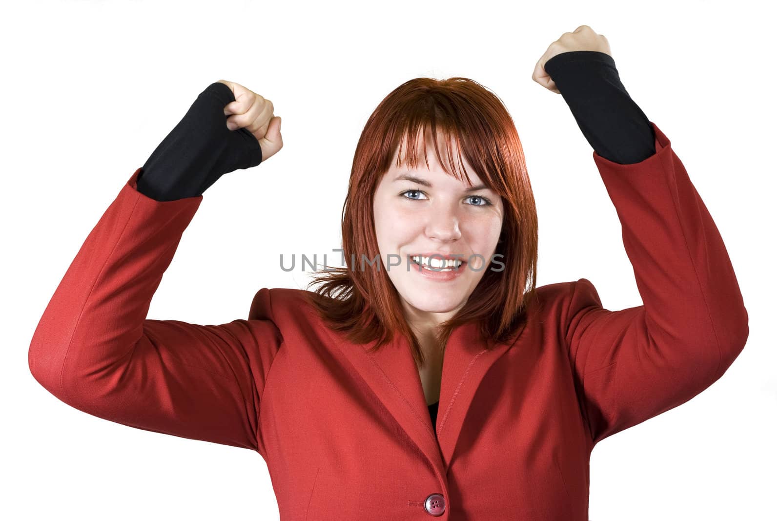 Cute girl with red hair dressed in a red business dress with her arms raised smiling and rejoicing for a win.

Studio shot.