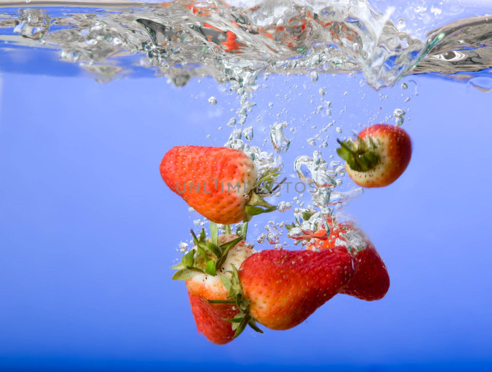 Strawberries falling in blue water with splash and bubbles