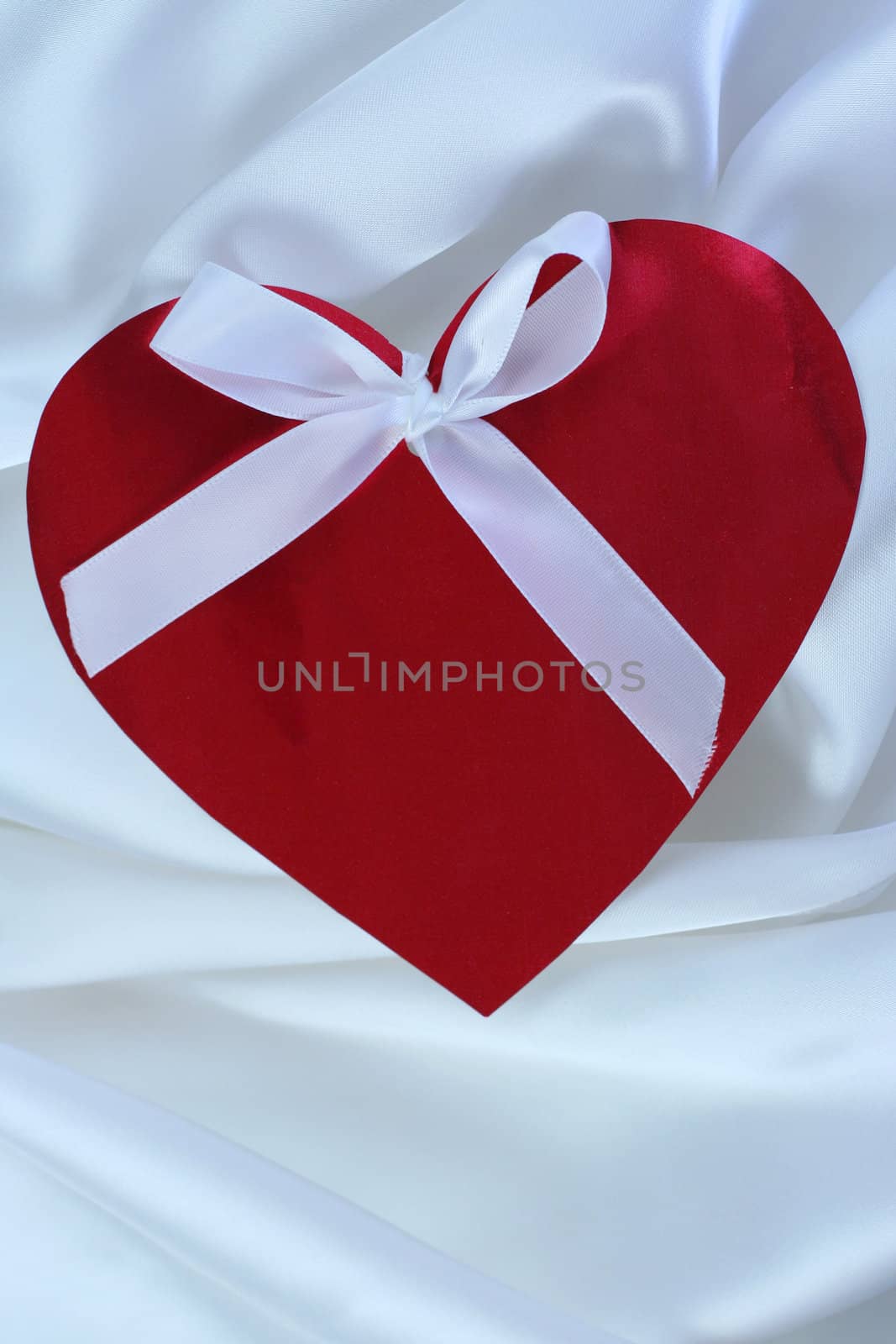Red heart with ribbon on white satin