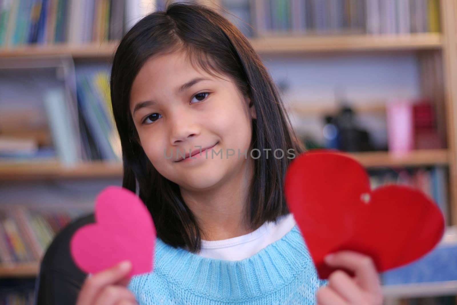 Nine year old girl holding up two red hearts.