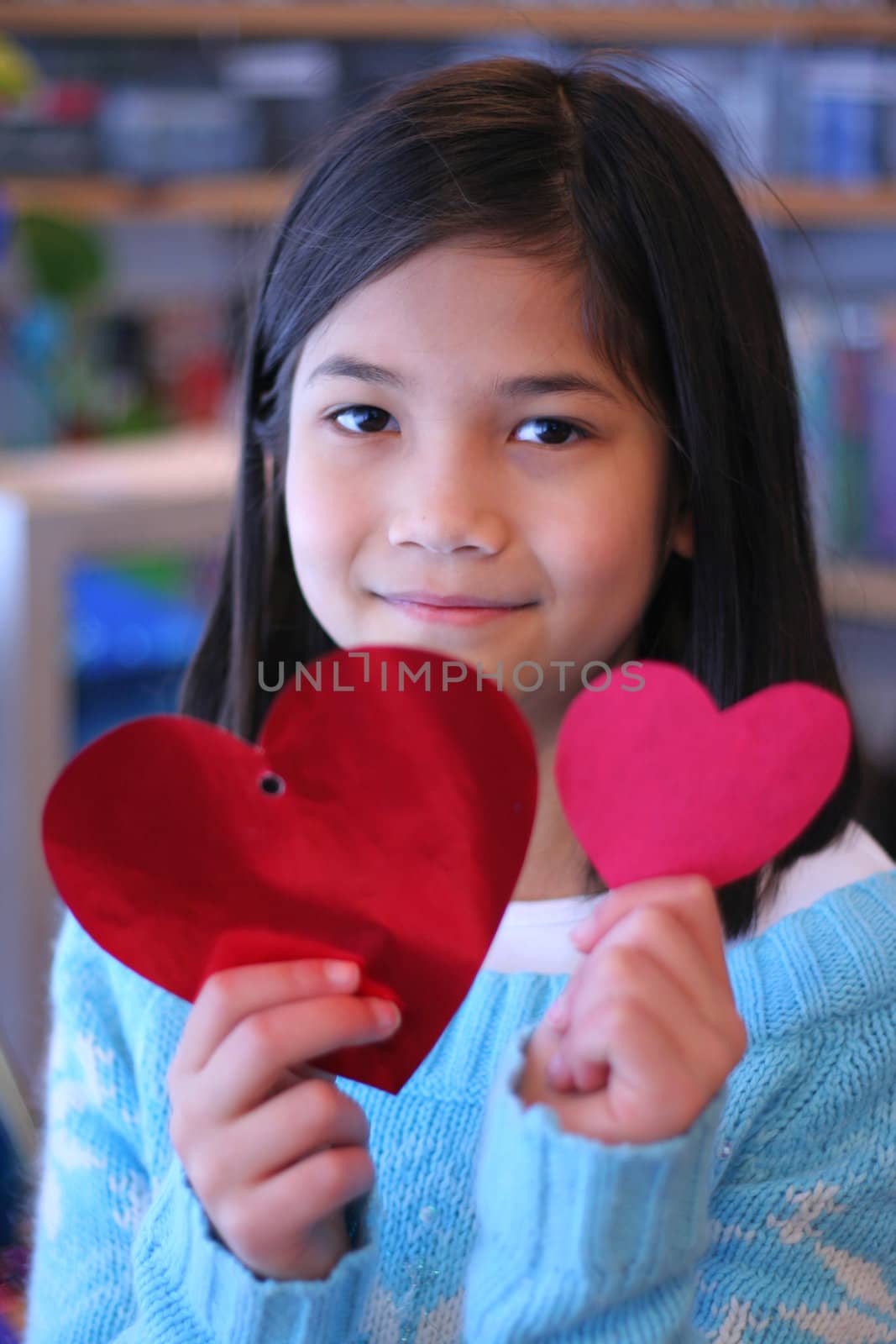 Nine year old girl holding up two red hearts.