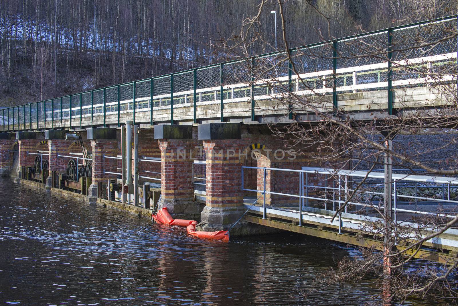 a footbridge that extends over the tista river at a place called "porsnes" in halden (halden is a city in norway), the bridge has a lock system that can regulate water flow in the river and the bridge foundations are bricked up in brick, the picture is shot one day in march 2013