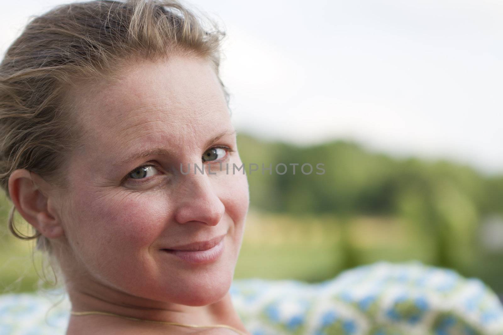 Beautiful Blond Turkish lady looking at the camera. Green blurry foliage at the background. No Make-up