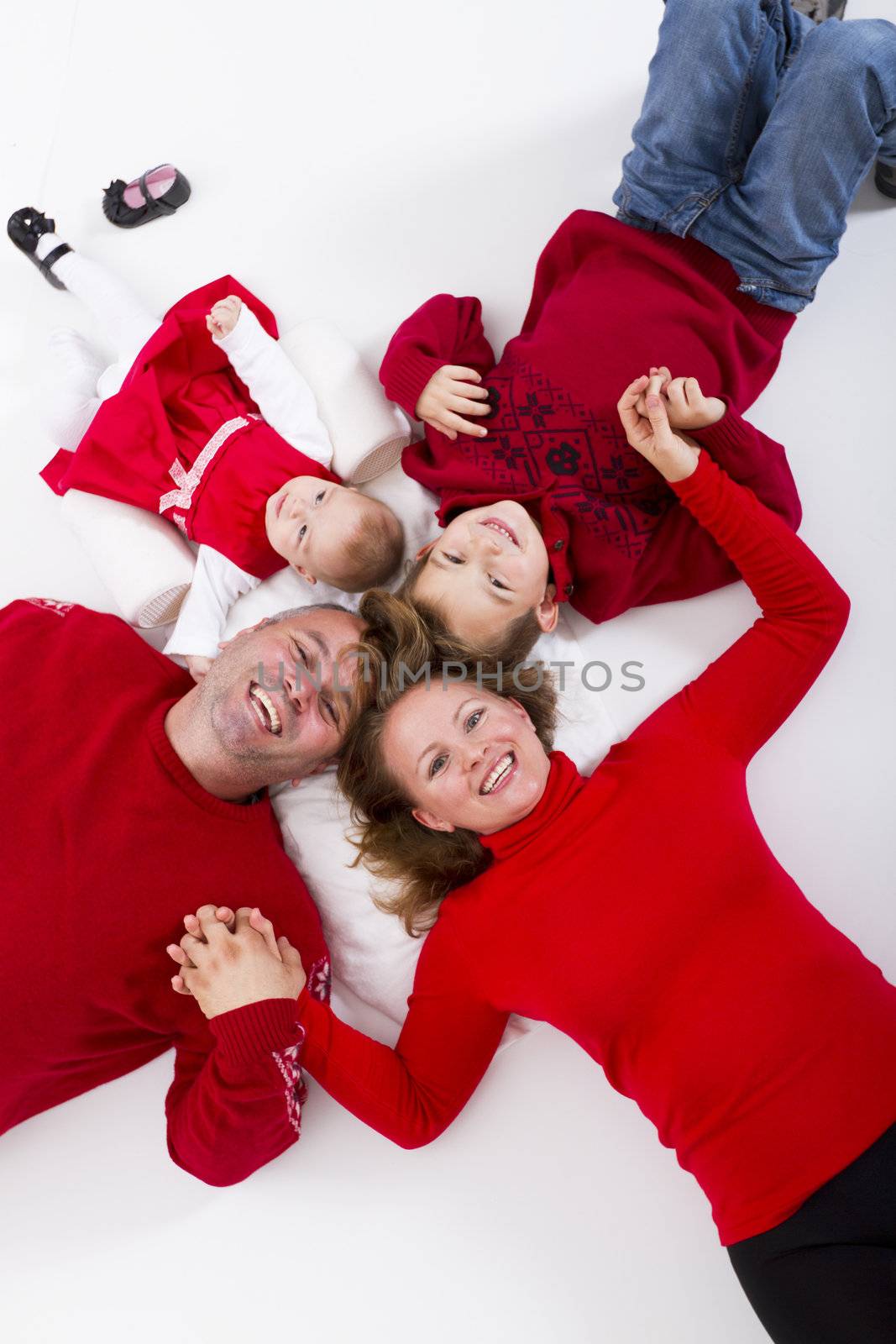 Girls and boys together as a family happily smiling to you on the floor hand to hand. 7 years old brother and 3 months sister and their happy parents.