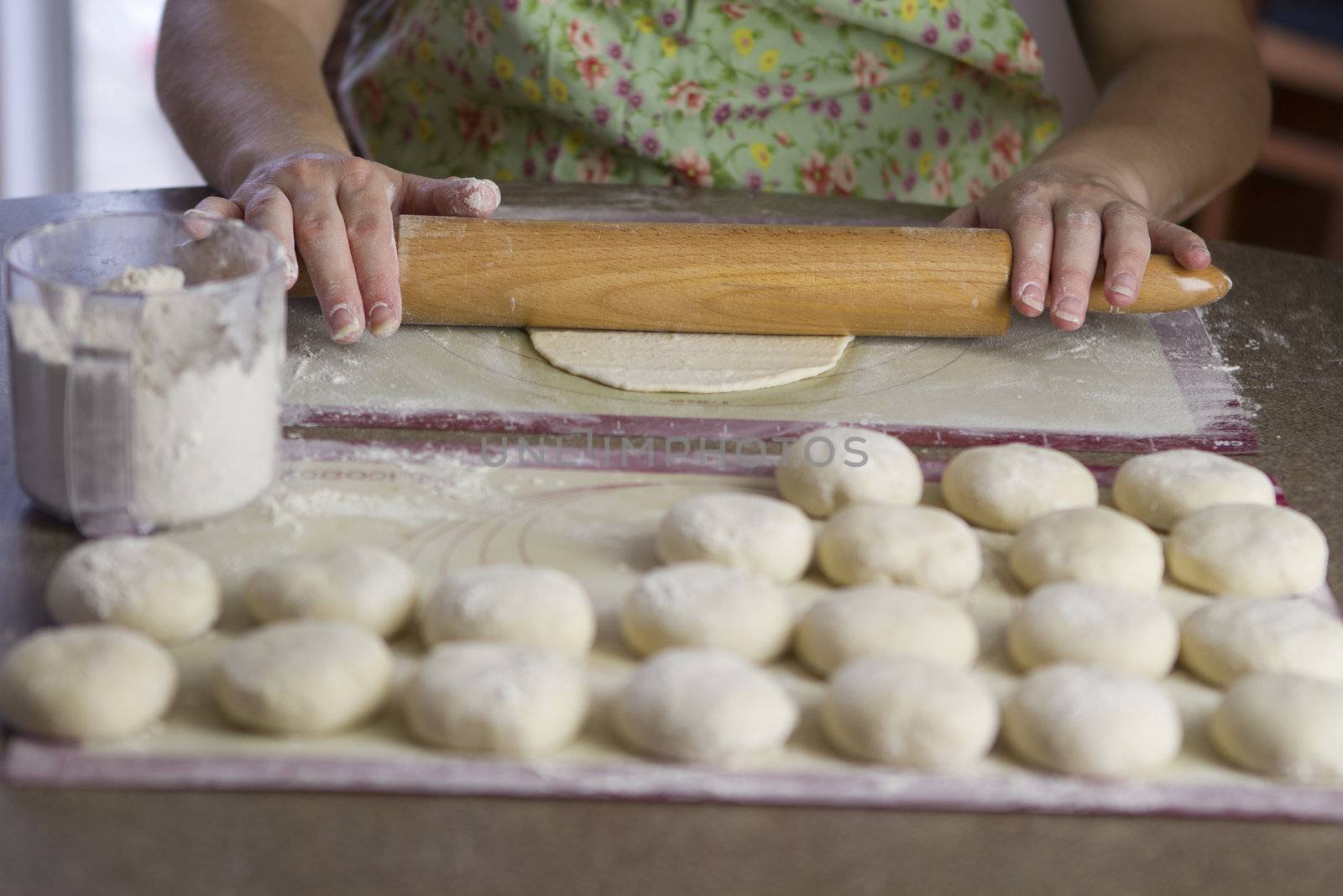 A lady flatten the dough to make flat bread pizzas using classic wooden roller.