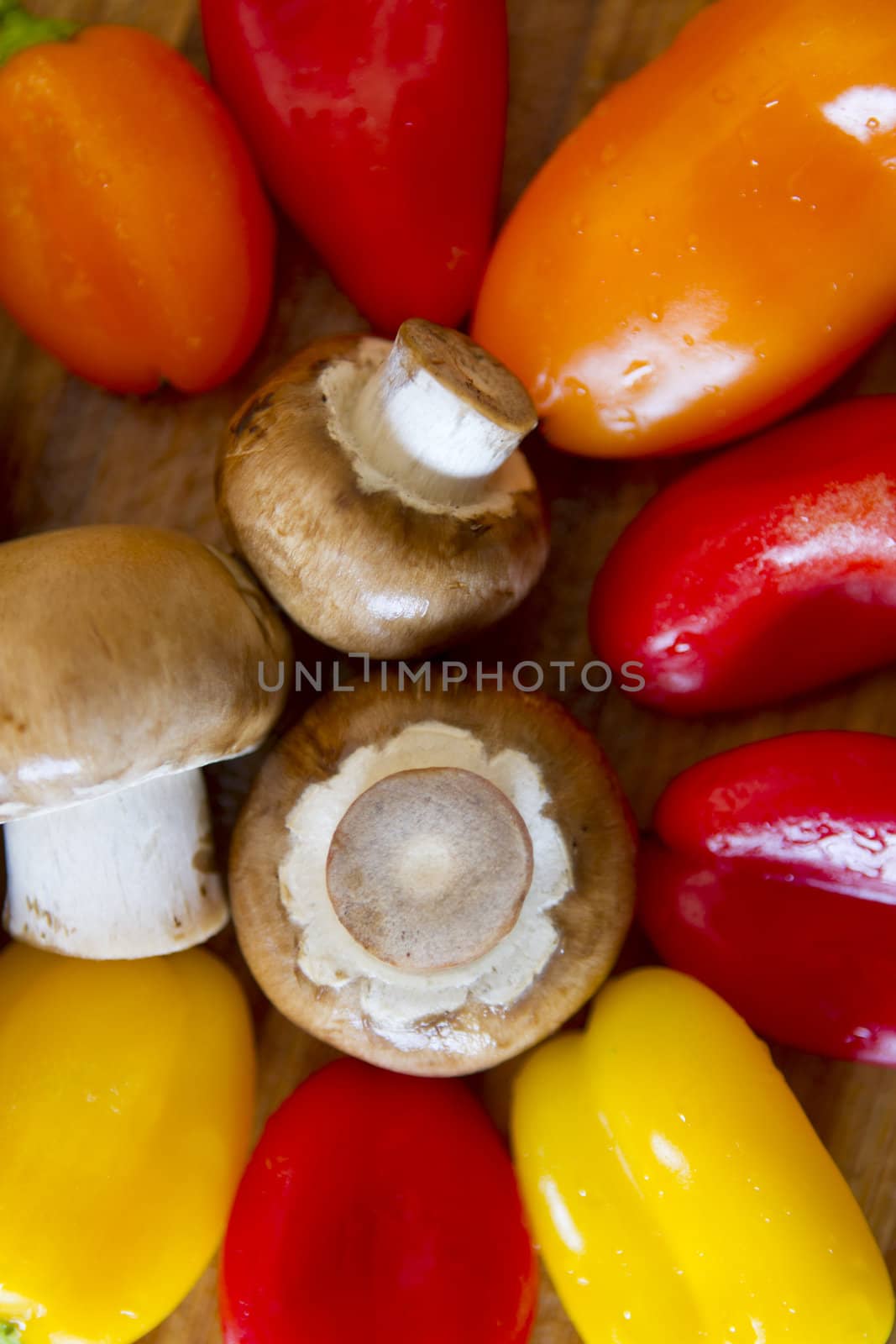Mushrooms and colorful peppers will get cut momentarily on a wet bamboo cutting board.