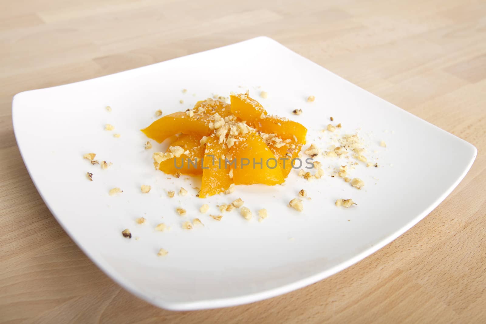 Home made Turkish traditional pumpkin dessert complimented with walnuts on large white plate on beech wood table.
