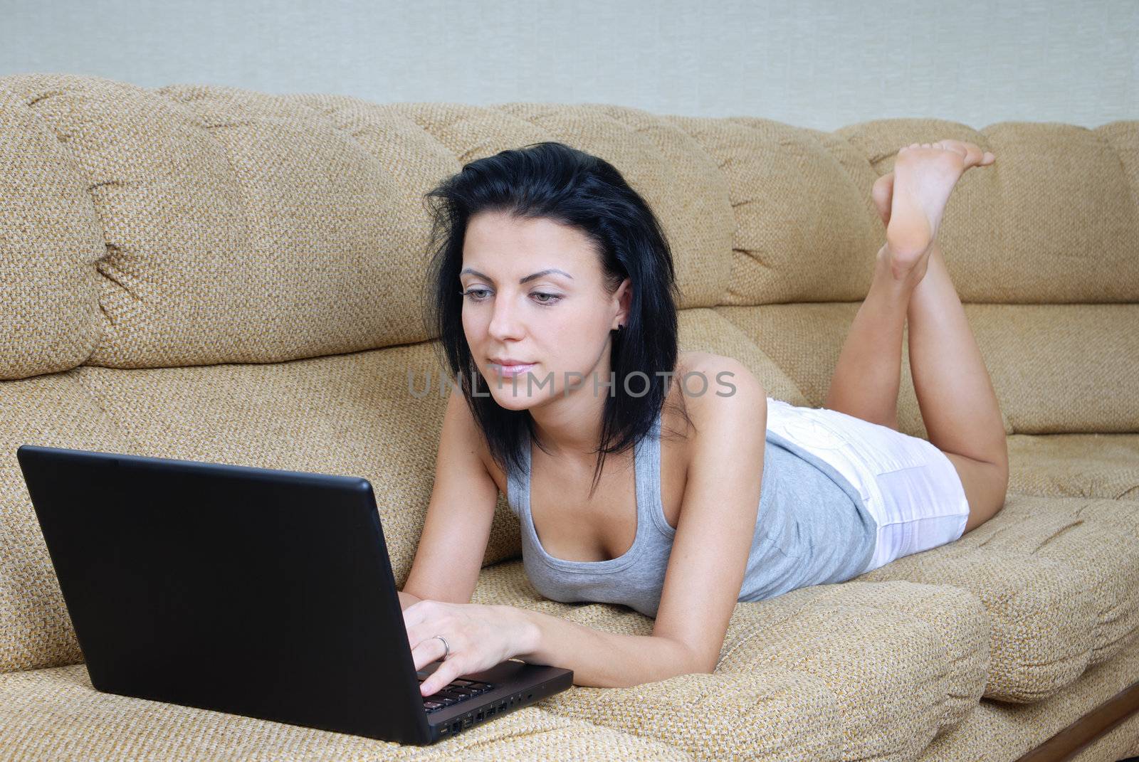 Serene lady laying on sofa and working a laptop