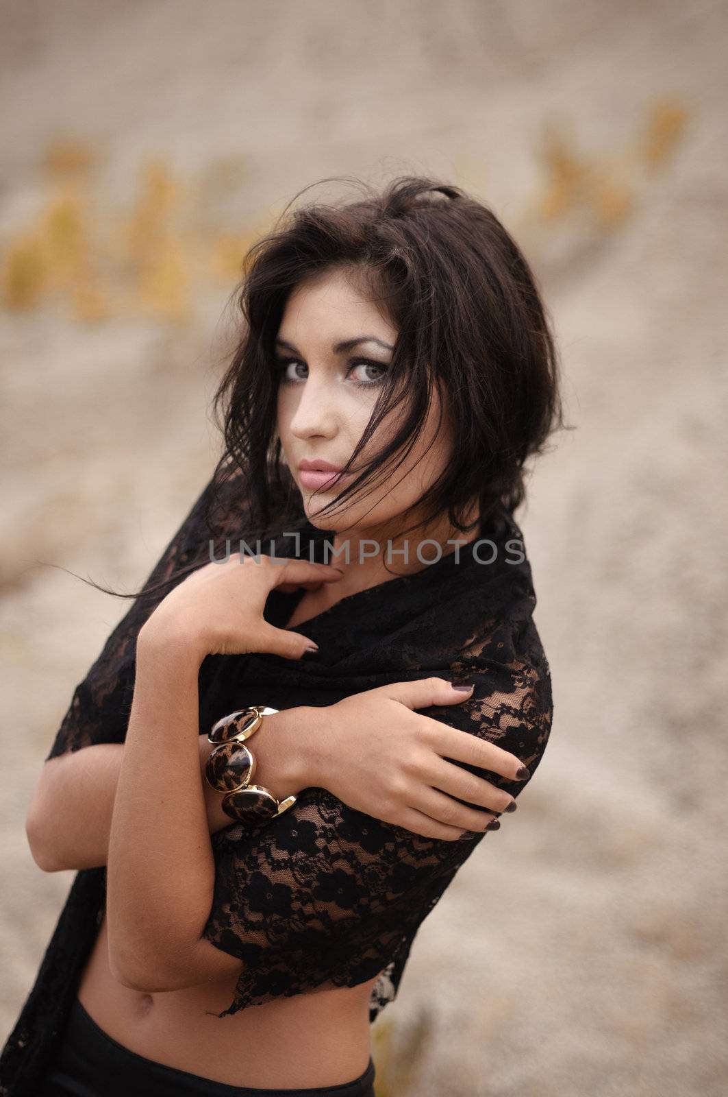 Woman in black lacy shawl looking sideways at the camera with serious expression, outdoor portrait.
