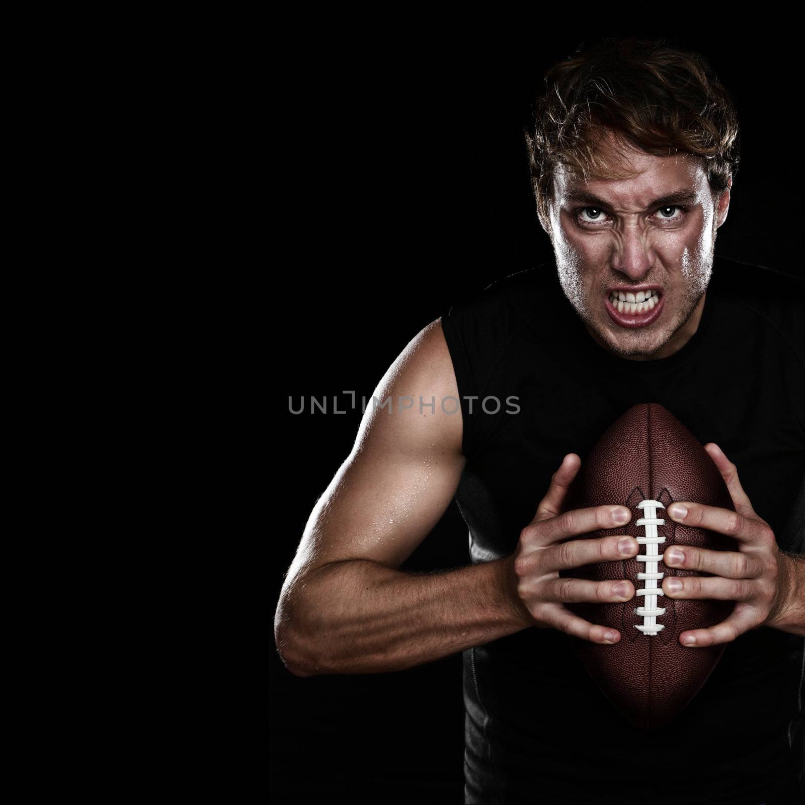 American football player staring aggressive holding american football on black background. Strong fit Caucasian fitness man with black copy space.