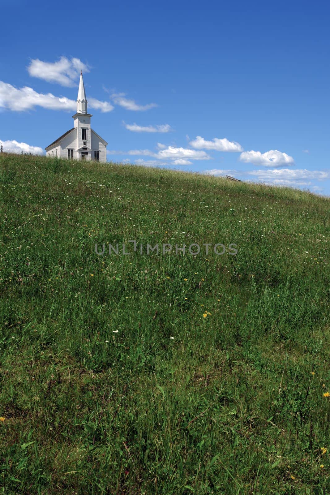 Photo of a little white wooden church on the top of a hill.