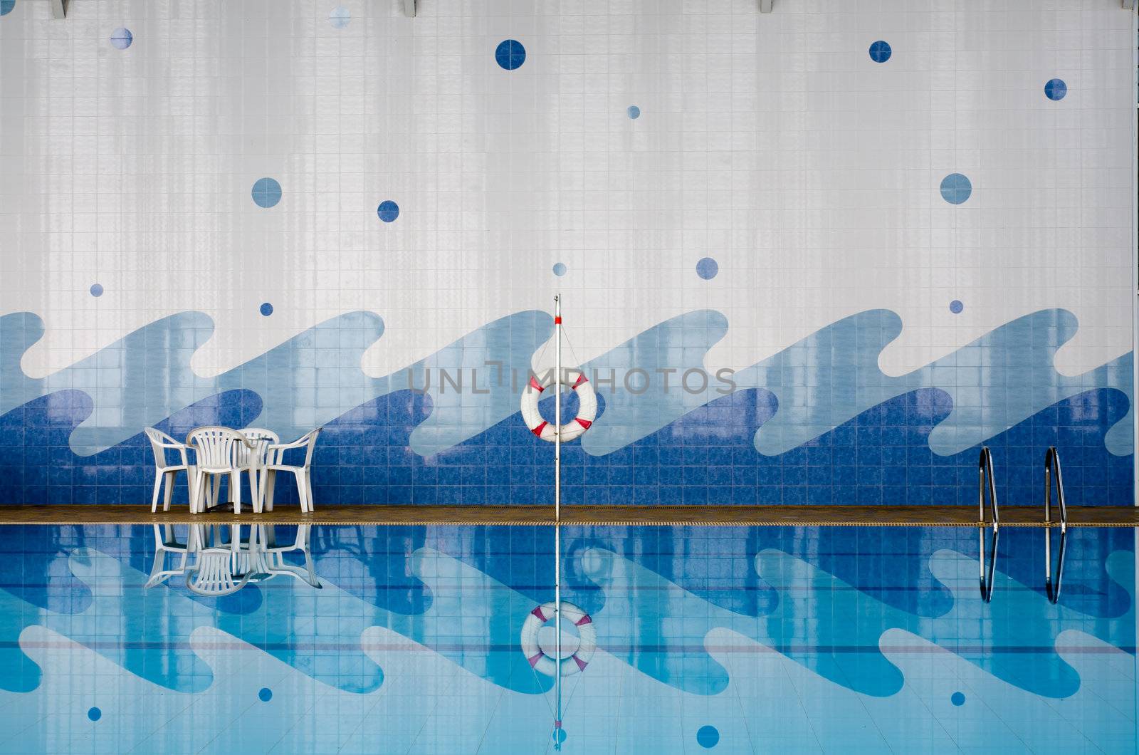 White plastic table and chairs, safety ring, ladder at pool side and reflect in water