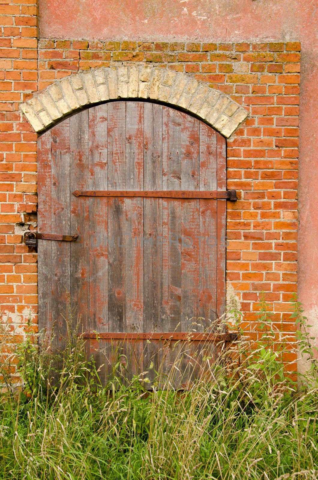 Old abandoned farm building doors locked with lock and tall grass. Red brick building background.