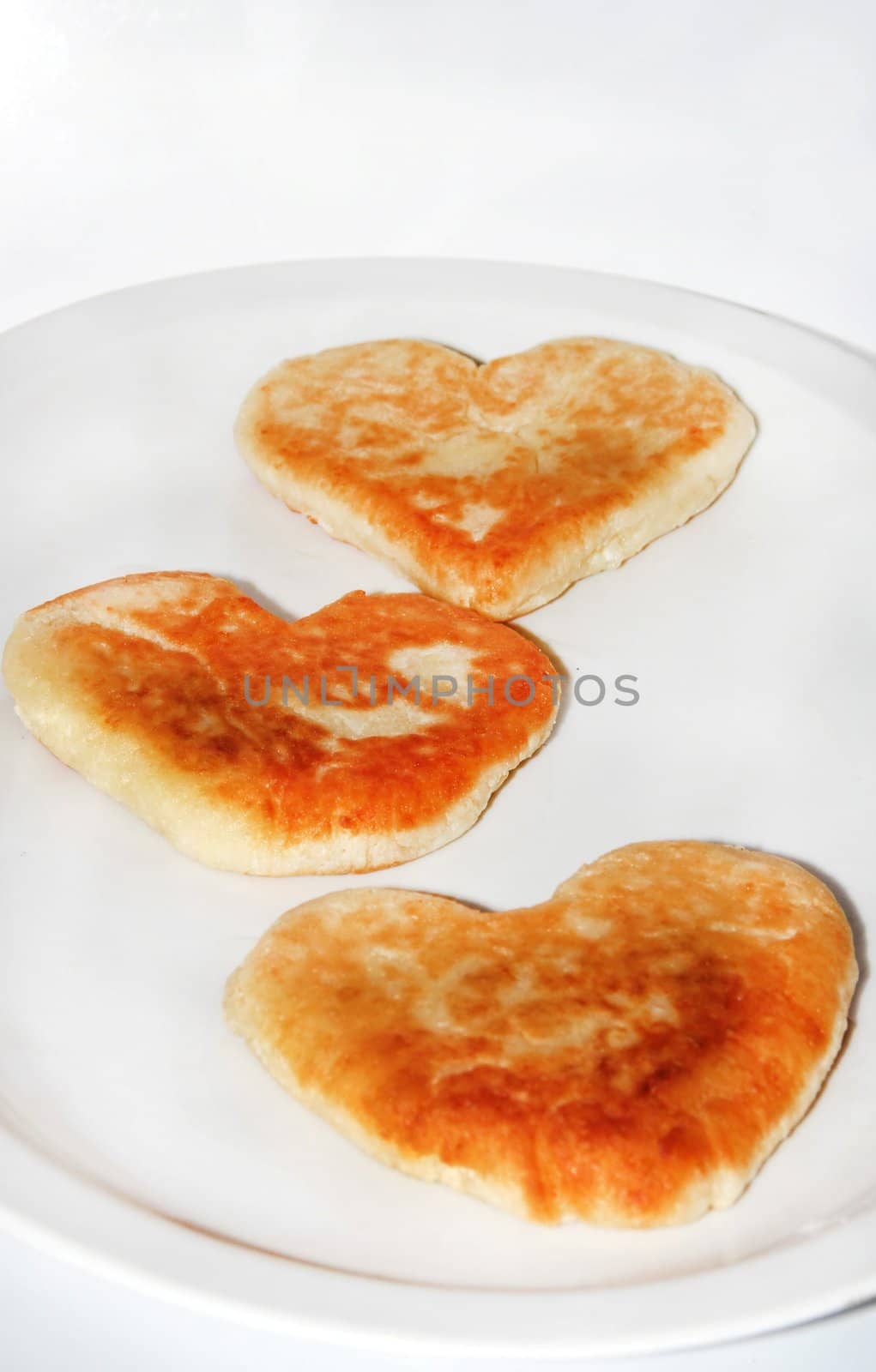 Cheese pancakes in form hearts. On a white dish and white background. Love