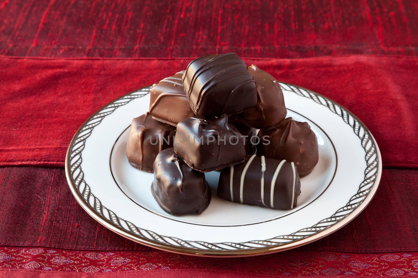 Dark and milk chocolate bon-bons on a white fine china plate with silver decoration on the rim. Red textured background.