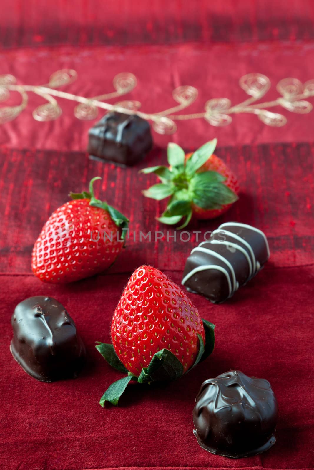 Dark chocolate bon-bons and strawberries on red textured background.