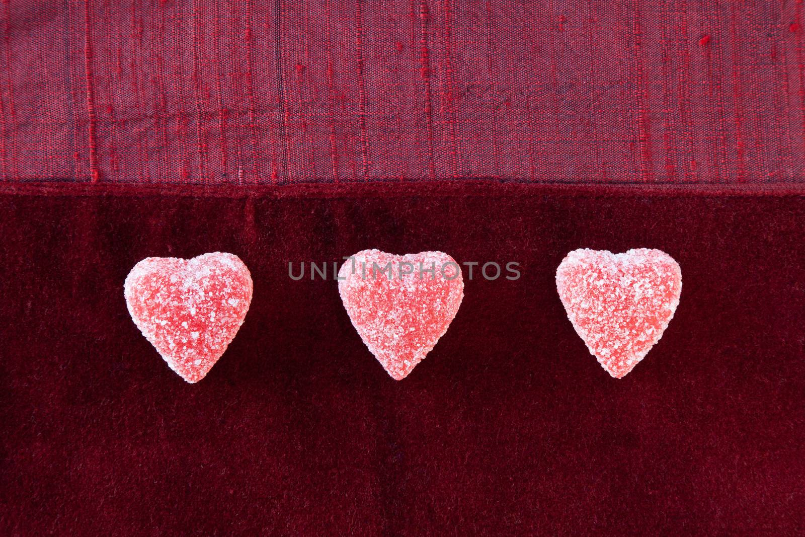 Three jelly (gummy) sugar coated candy hearts in a row on red textured background.