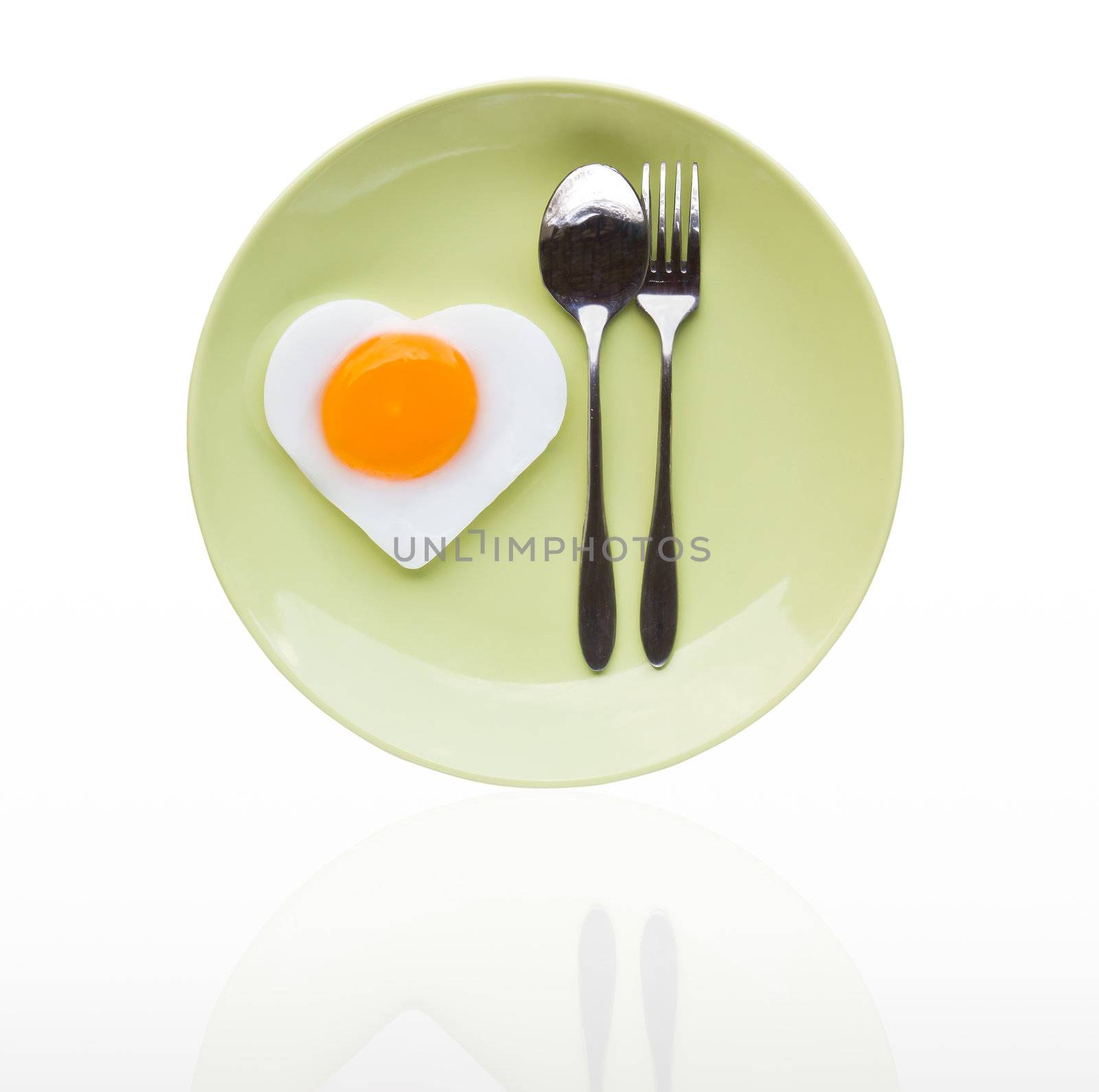 Fried egg heart and spoon on green dish