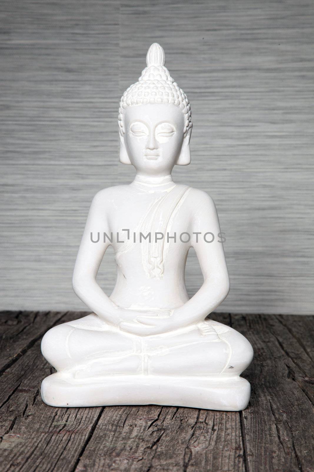 Indoor white seated statue of Buddha sitting in the lotus position with clasped hands meditating and praying on weathered timber boards