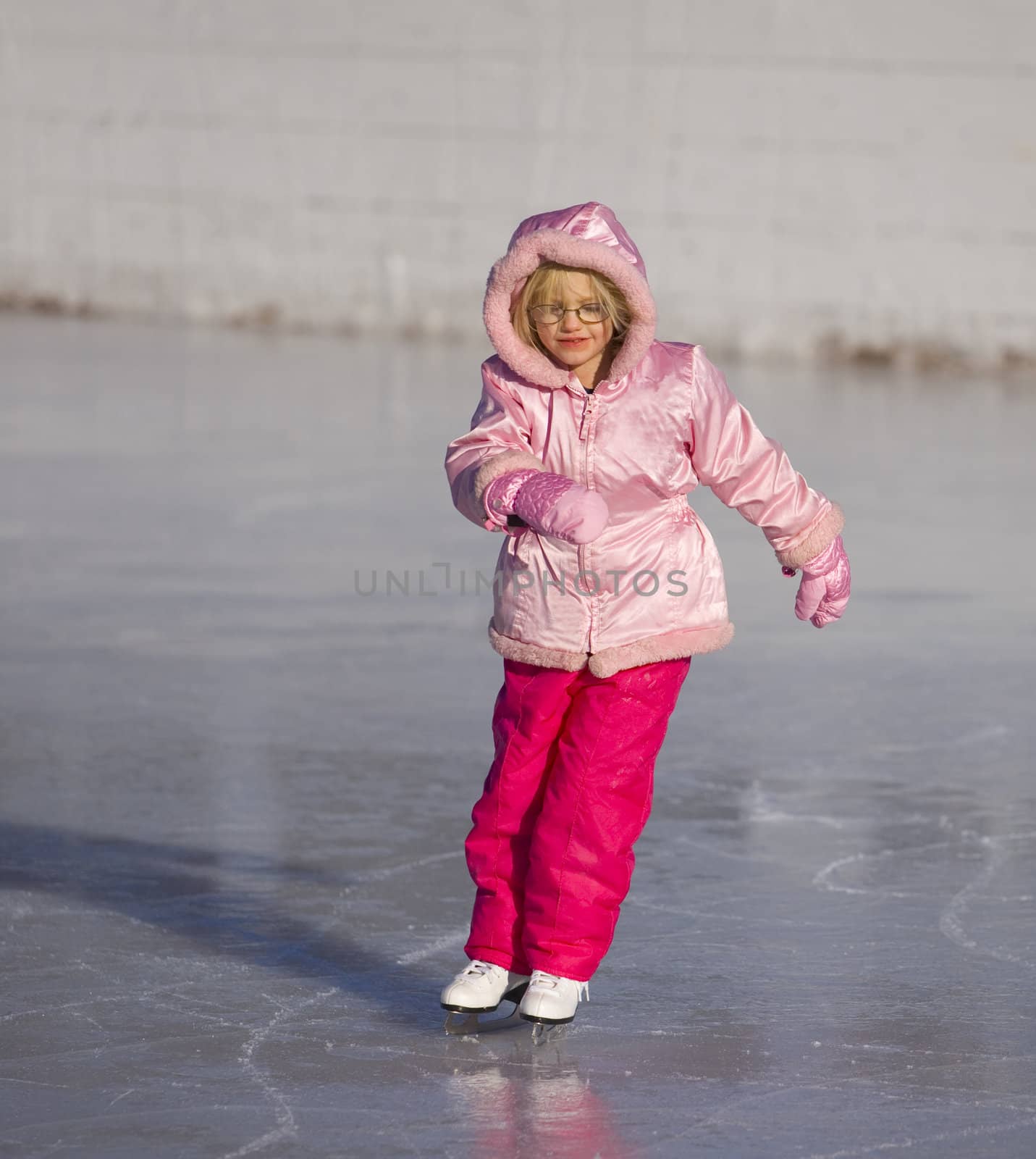 Child in pink ice skating and leaning into a curve