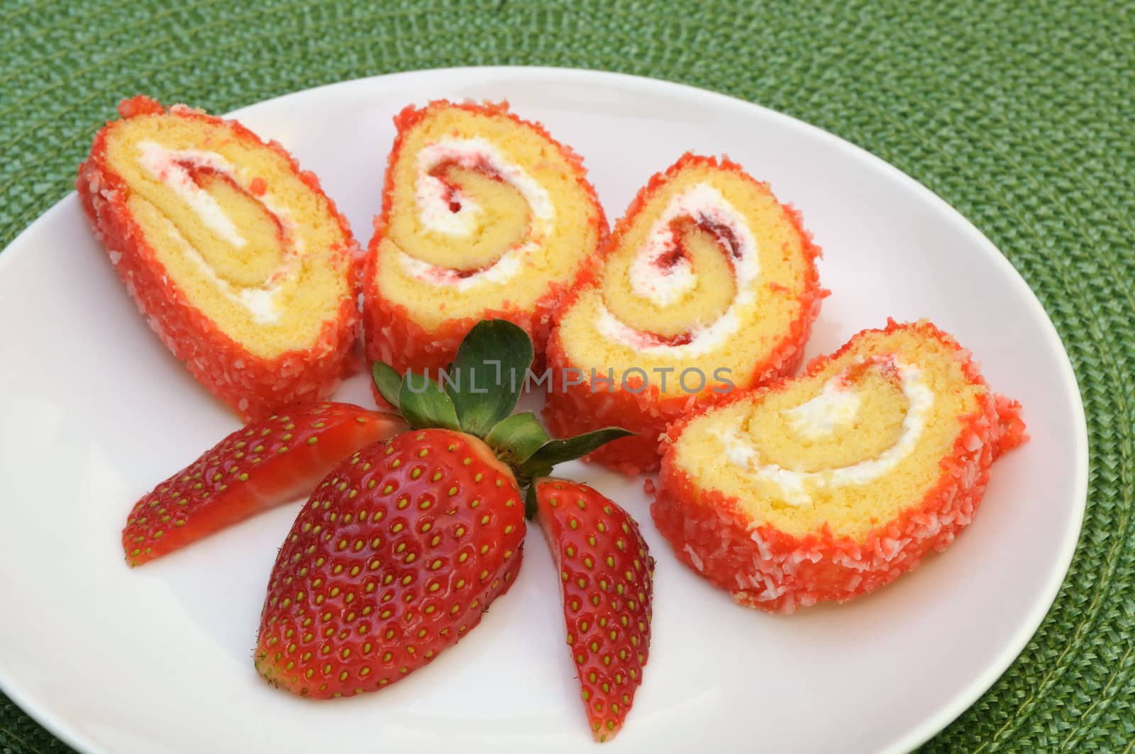 Jam roll cake slices decorated with strawberry on a green mat