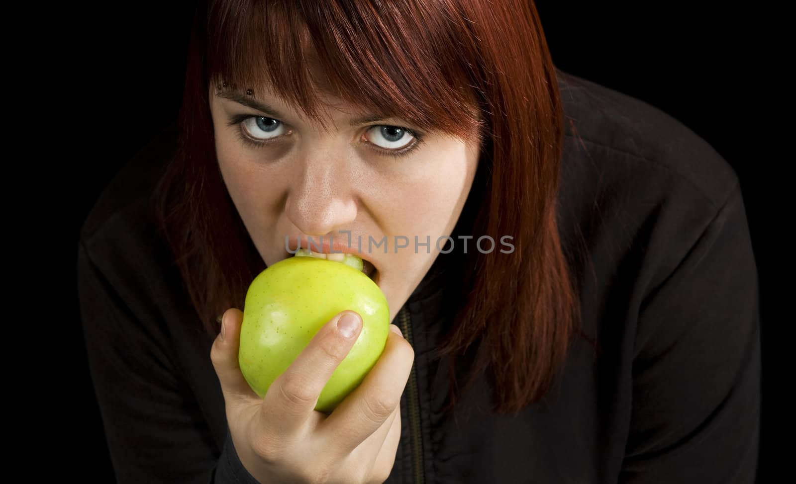 Redhead girl biting on a delicious green apple with a flirtatious look.

Shot in studio.