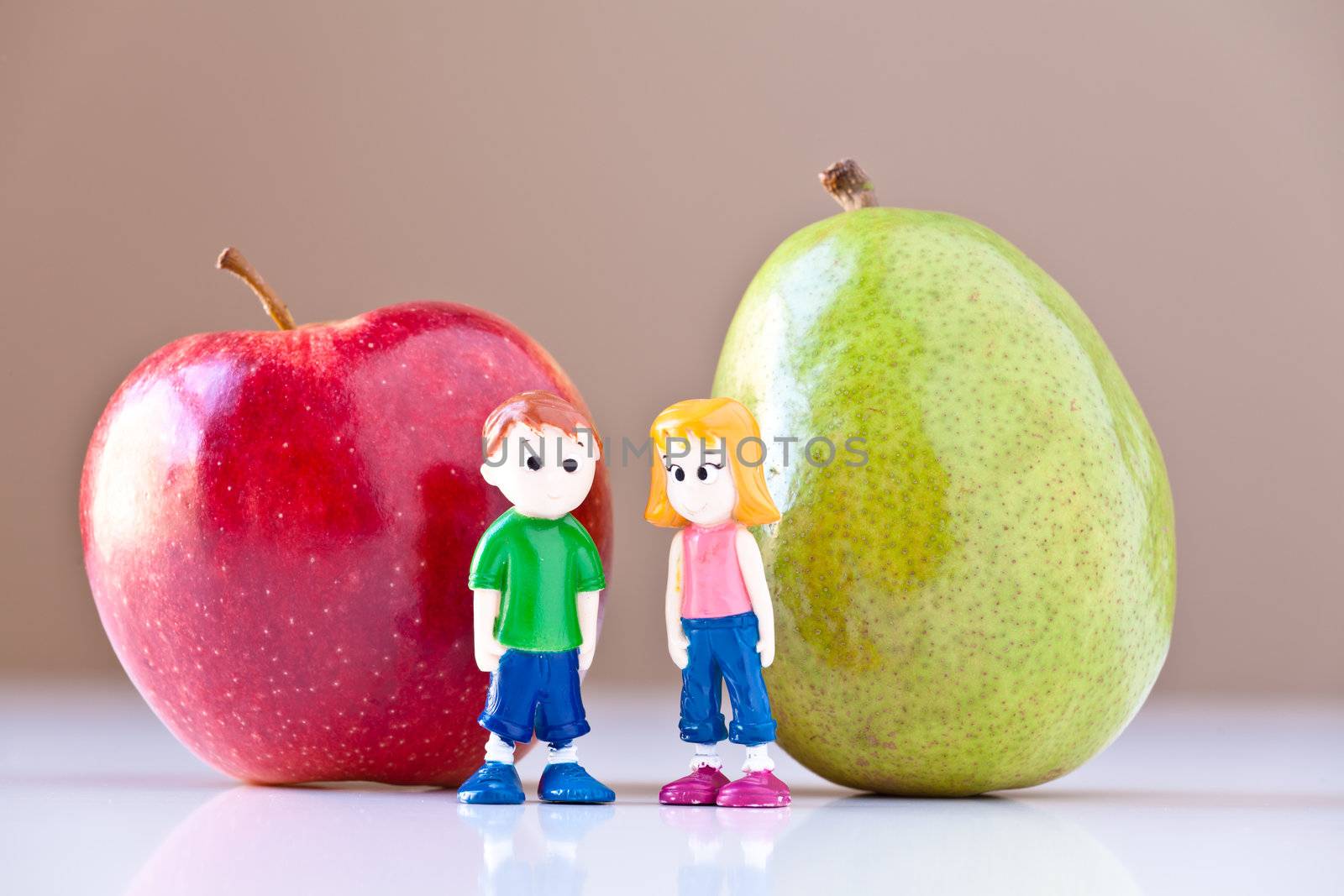 Toy girl and boy discuss nutrition and healthy choices in front of a green pear and a  red apple. The concepts depicted in this image are nutrition, good food choices, balanced diet and good for you.