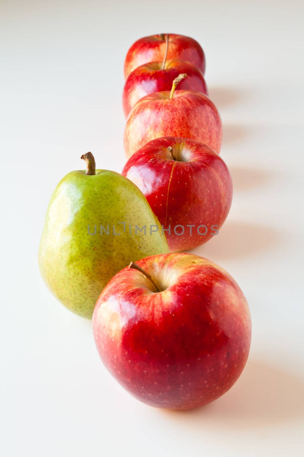 Green pear standing out from a line of red apples. The concepts depicted in this image are nutrition, good food choices, balanced diet, good for you, being different, unique, stick out, being singled out.