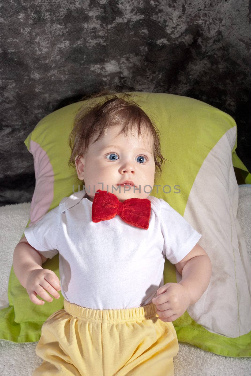 Happy baby in the red tie sitting in a studio.