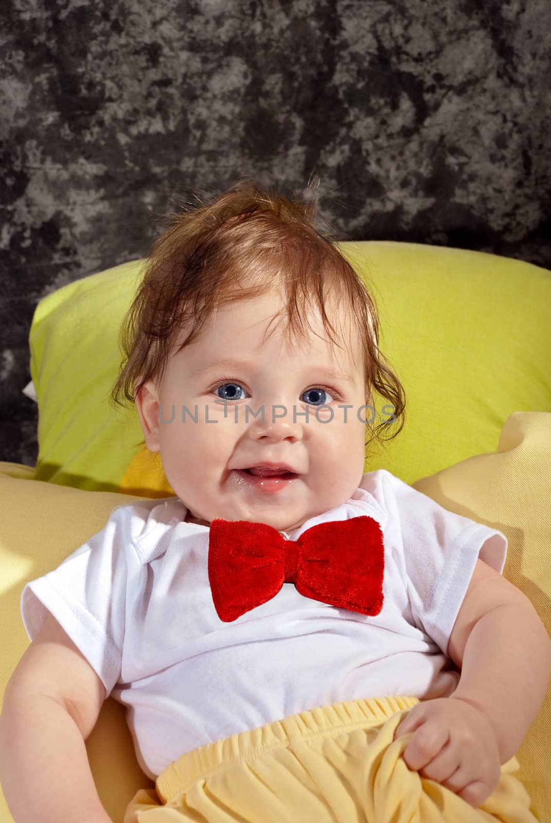 Happy baby in the red tie sitting in a studio.