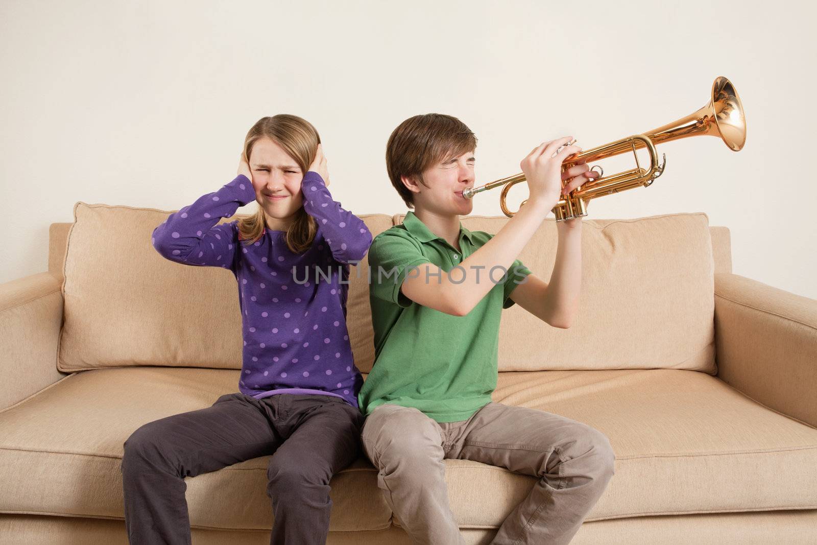 Photo of a brother playing his trumpet too loudly, or badly, and annoying his sister.