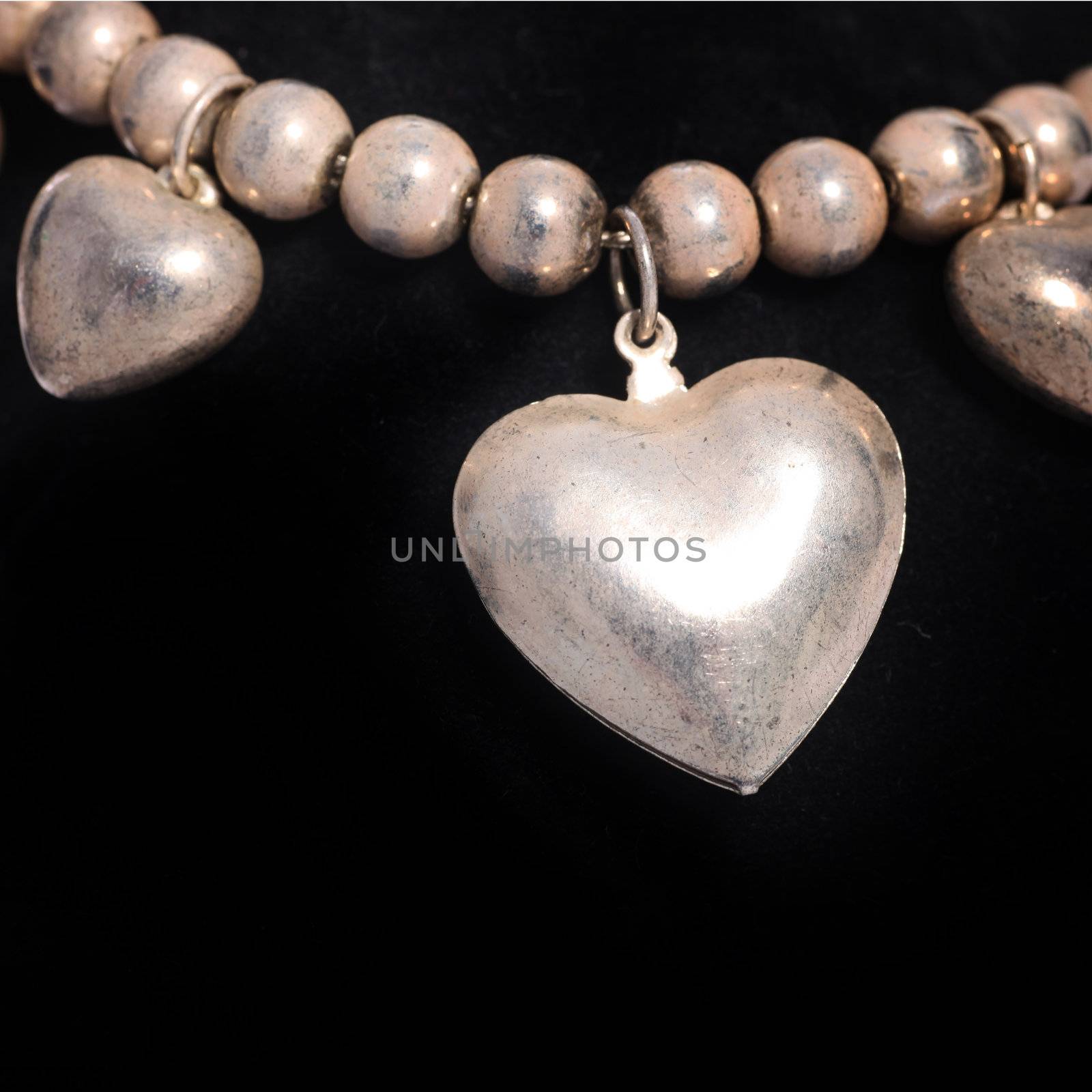 Necklace of round silver beads interspersed with hearts of different sizes isolated on a black studio background