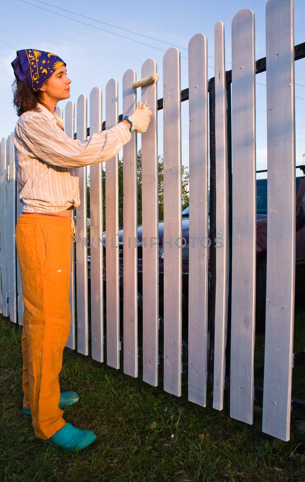 Beautiful girl colours the wooden fence at sunset by nikolpetr