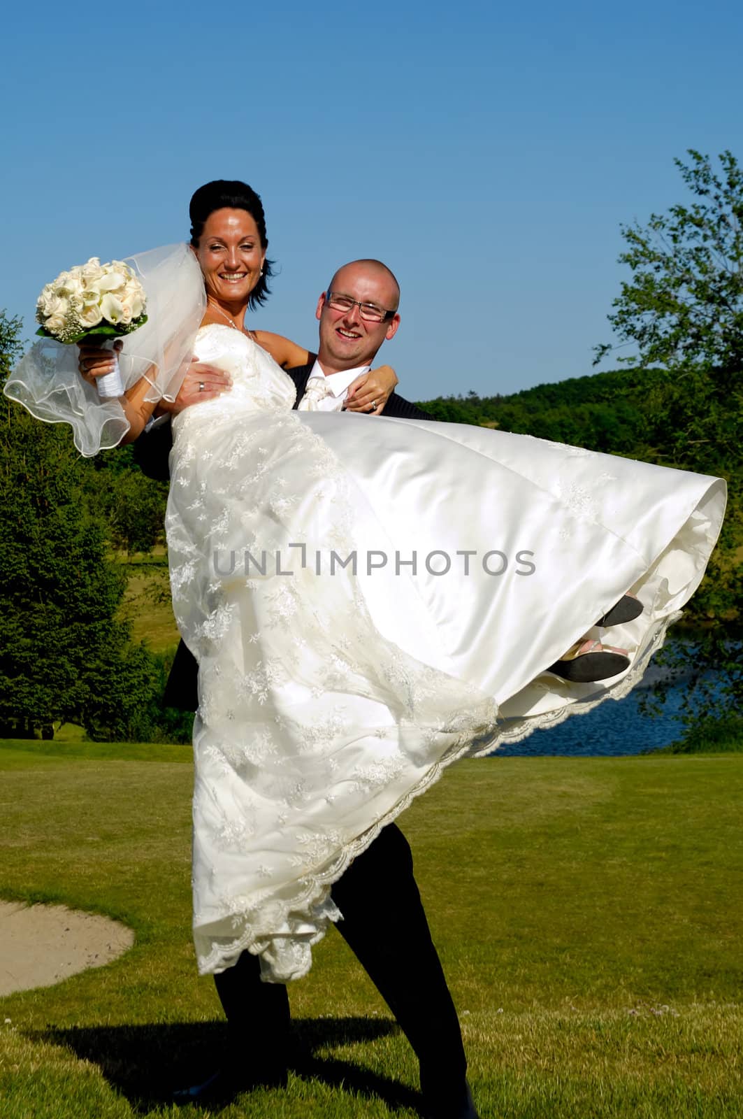 Groom is lifting his bride up in a park.