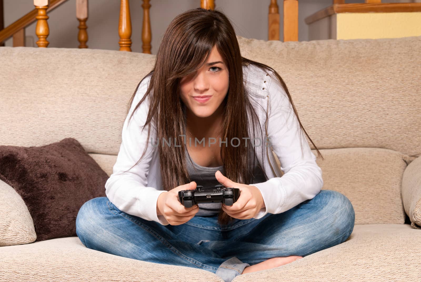 Young female playing video-games concentrating on sofa at home by dgmata
