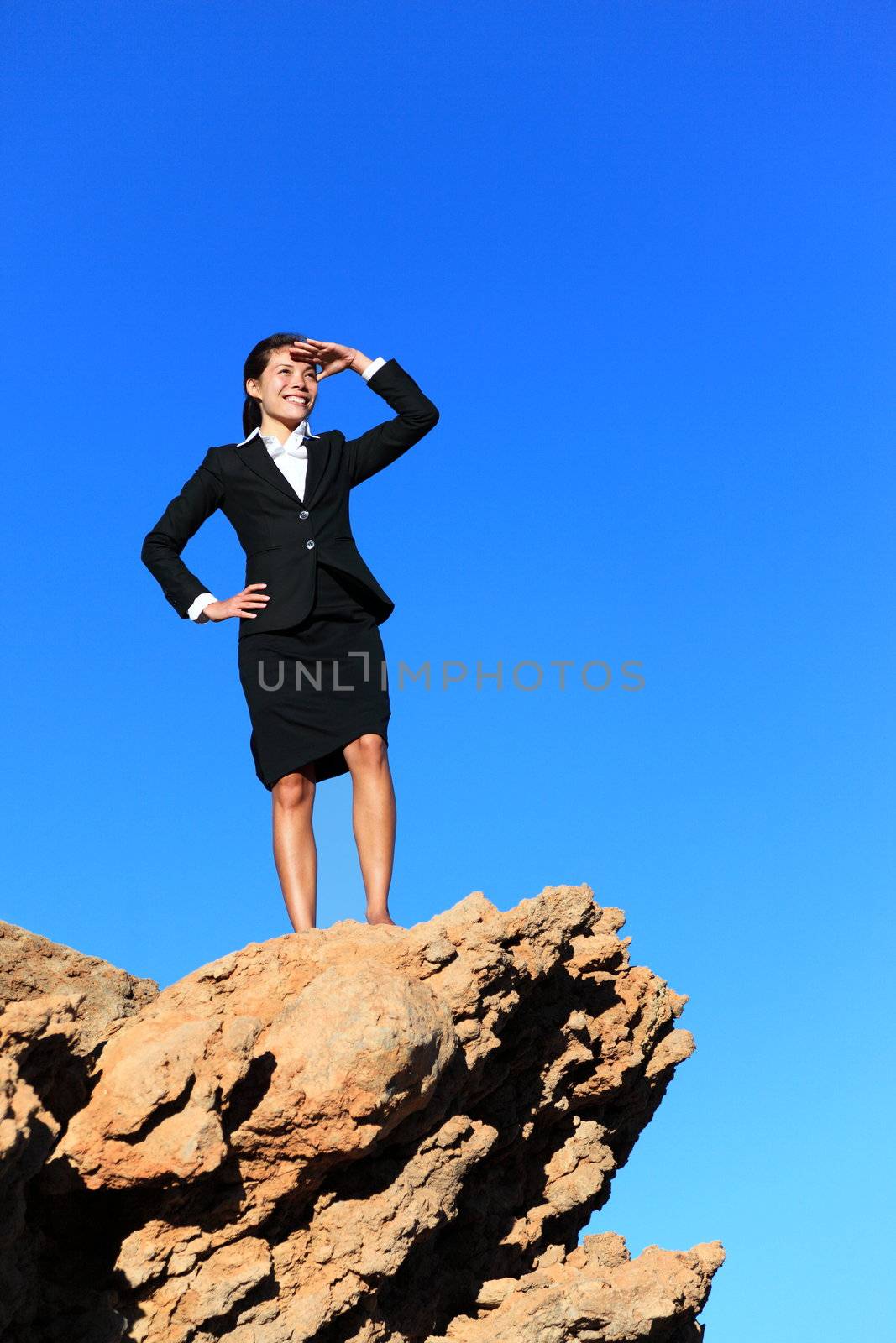 Business woman looking from mountain top. Business future concept image - businesswoman looking at horizon. Young multiracial executive.