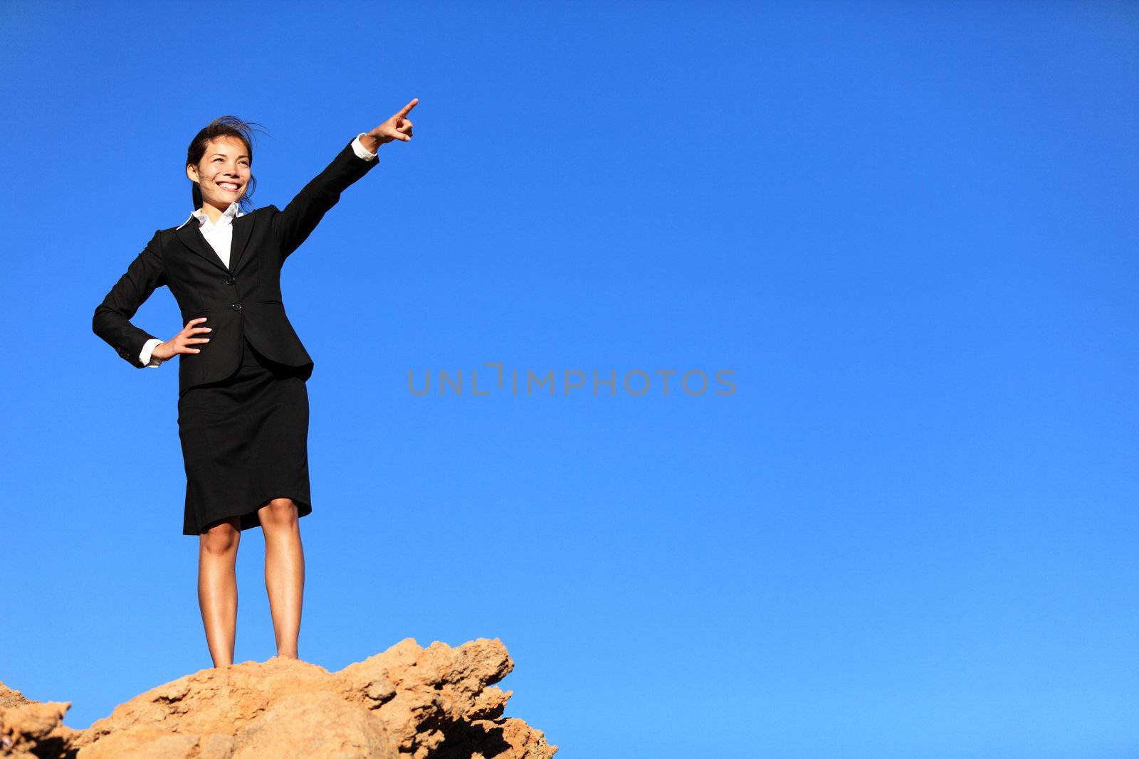 Business concept - businesswoman pointing at future ahead standing on mountain top wearing suit.
