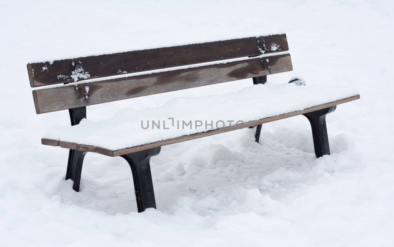 Wooden bench covered in snow in snow-covered park.