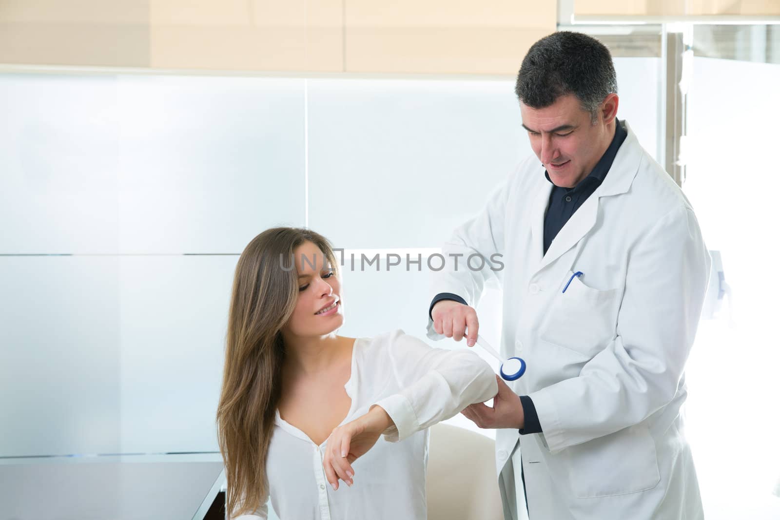 Doctor checking elbow with reflex round hammer to woman patient in hospital