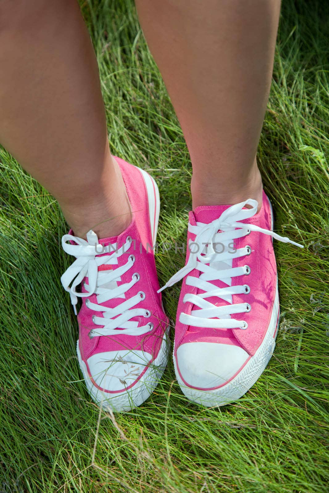 Pink sneakers on girl legs on grass by photocreo