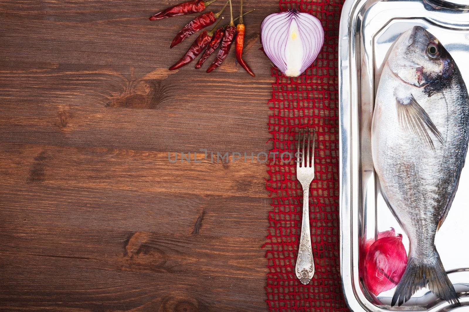 Dorado fish on a wooden surface with red onion and pepper