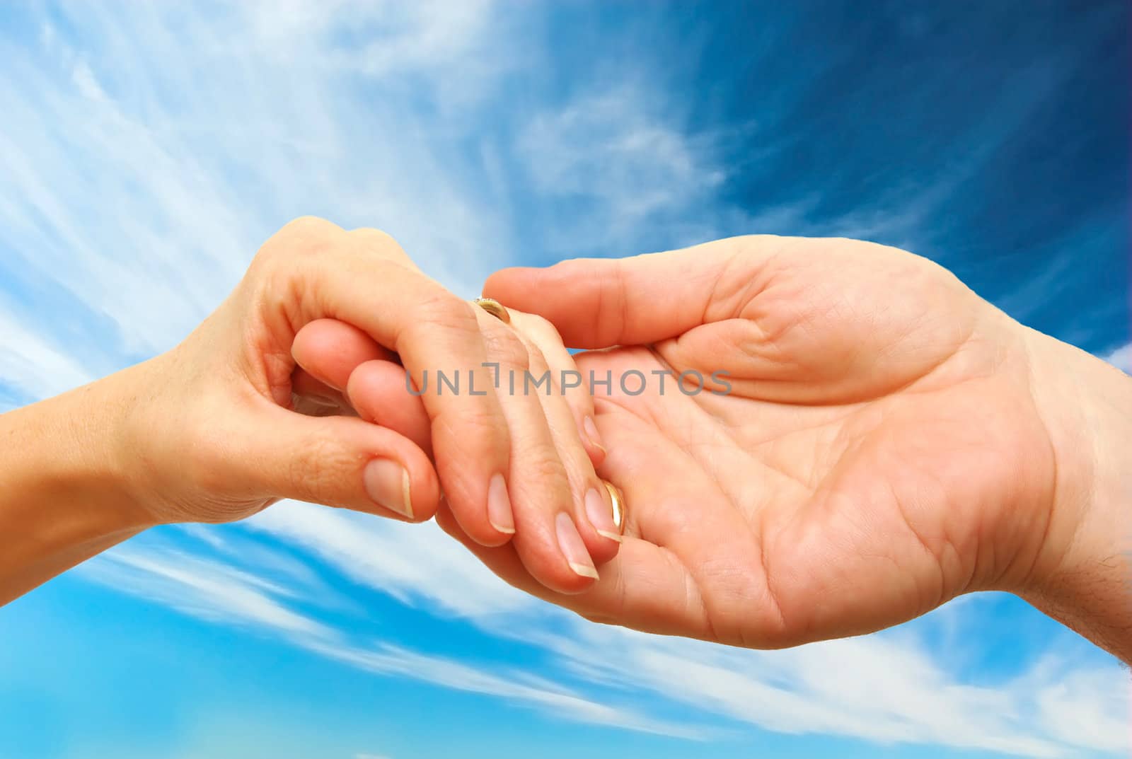 Two hands - woman and man touch each other in delicate, subtle way on sky background
