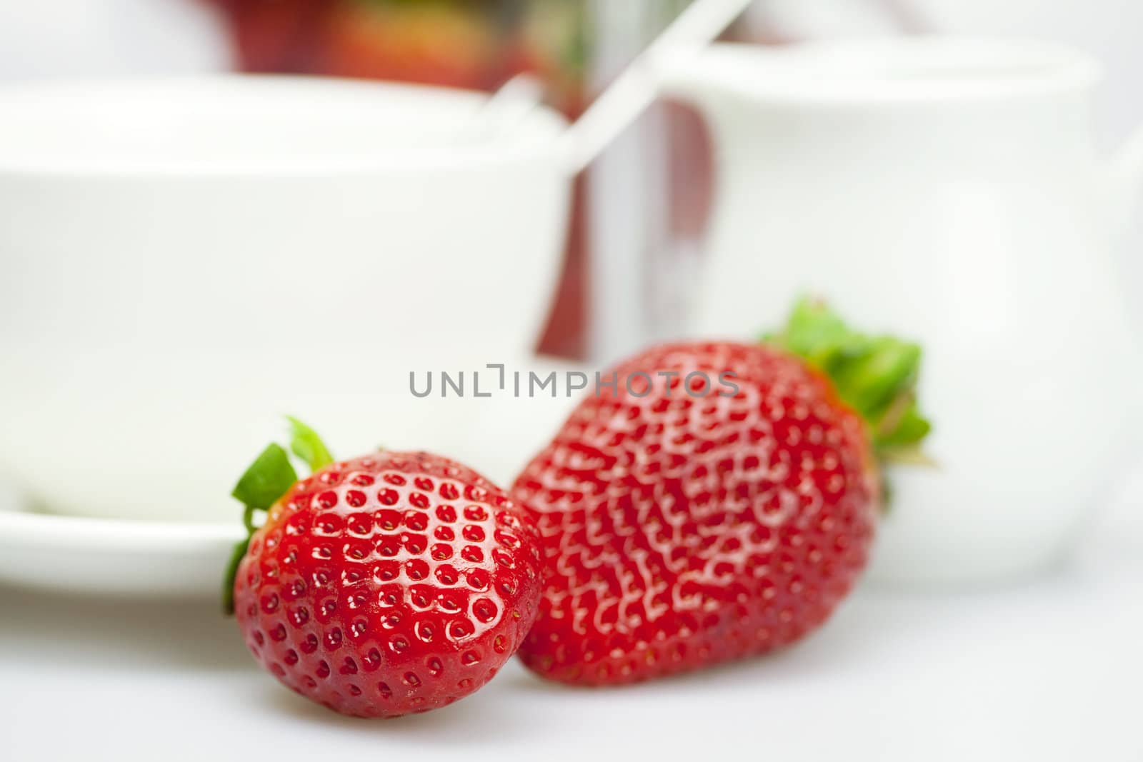 white cup and milk jug with strawberries isolated on white by jannyjus