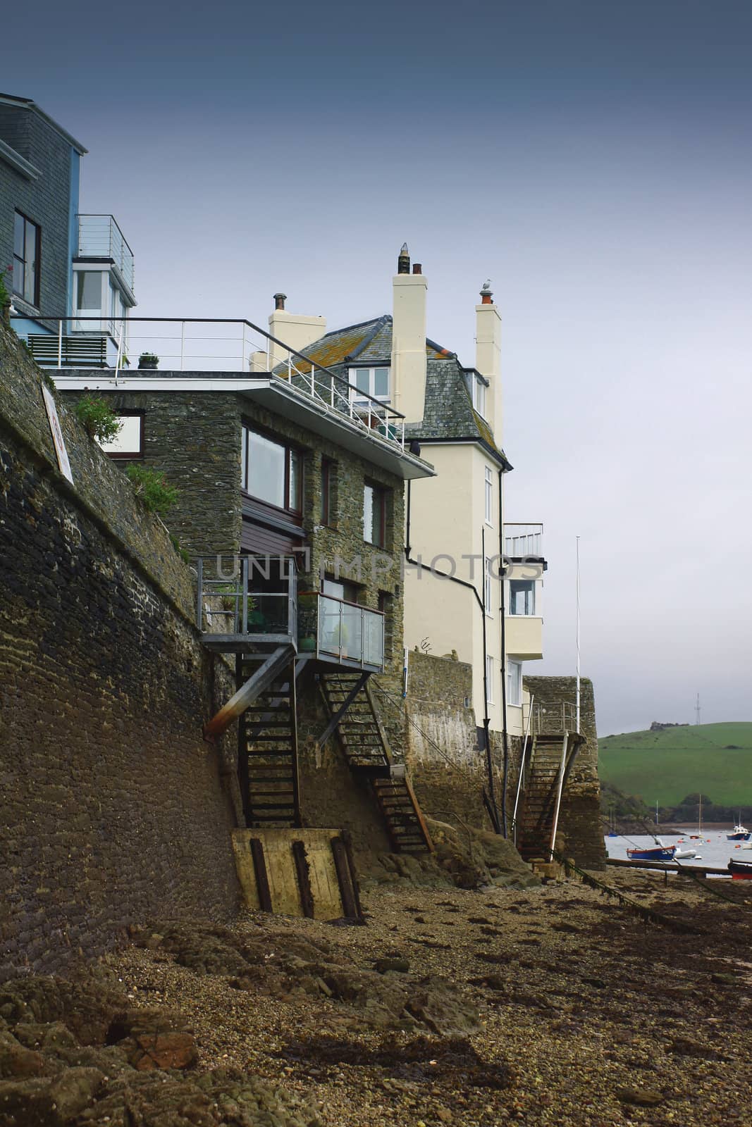 Low tide at Salcombe in devon. A portrait format image showing sea shore buildings with access to the shore via stairways.
